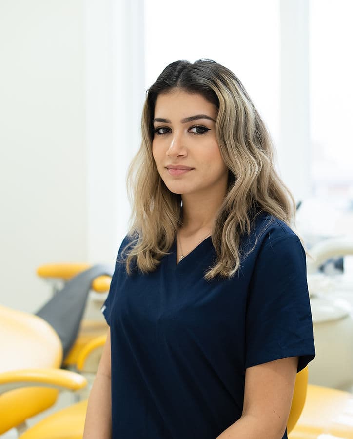 Sarit, dental assistant, in navy scrubs beside a yellow dental chair